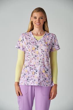 A floral print scrub top in lavender with yellow flowers, paired with a light yellow long-sleeve shirt and purple pants.