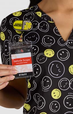A patterned shirt featuring various smiley faces in yellow and white on a black background, held by a person with a badge.