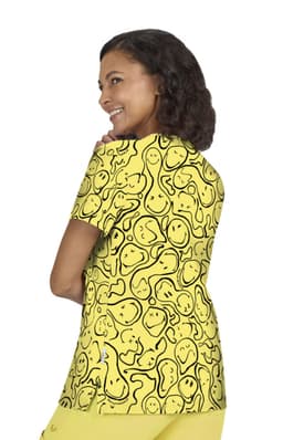 A vibrant yellow T-shirt featuring a playful pattern of smiling faces. The model is shown from the back and has curly hair.