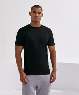 A black organic T-shirt displayed on a male model, paired with grey sweatpants. The garment features a logo.