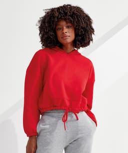 A red cropped oversize hoodie with a drawstring hood, paired with grey pants, featuring a logo on the fabric.