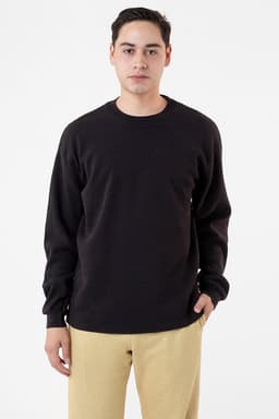 A man wearing a black heavyweight thermal crewneck jumper paired with beige trousers. The garment has a logo on it.