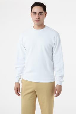 A man wearing a white crewneck sweater, styled with beige trousers. The sweater features long sleeves and has a logo.