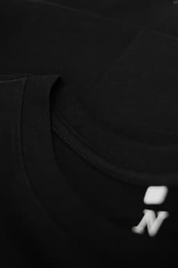 A black T-shirt featuring a rounded neckline and a logo on the hem. The fabric appears soft and smooth.