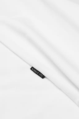 A white t-shirt with a small logo tag partially visible, set against a smooth fabric background.