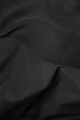 A hybrid jacket featuring a mix of textured and smooth black fabric, with a logo present on the product.