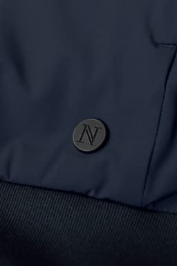 A navy hybrid jacket featuring a textured fabric and a logo badge on the front.