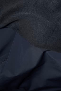 A hybrid jacket featuring a textured black upper and a smooth navy lower section, with a logo present.