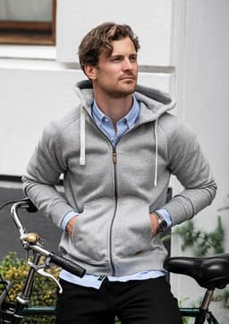 A grey hoodie with a zipped front and drawstrings, worn by a man sitting beside a bicycle.