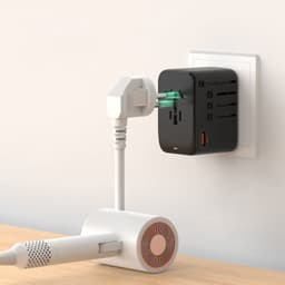 A black travel adaptor with multiple ports is plugged into a wall socket, connected to a white device.