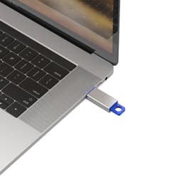 A silver and blue flash drive is plugged into a laptop's USB port, with the laptop keyboard visible in the background.
