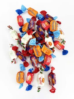 A collection of colourful mixed lollies in various wrappers, featuring blue, red, and white designs, with a logo present.