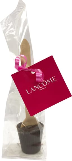 A chocolate spoon in a clear bag with a wooden stick, featuring a pink ribbon and a branded tag.