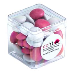 A clear cube container filled with pink and white chocolate-coated beans. The container has a label and branding.