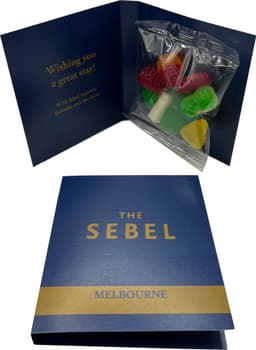 A gift card with a blue cover opens to reveal a bag of mixed lollies in various colours, including red, green, and yellow.