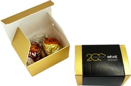 A gold and white box containing two chocolate balls, featuring branding on the exterior.