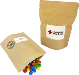 A compostable bag containing colourful M&Ms spilling out, with a simple natural kraft design and a logo.