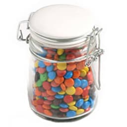A glass clip lock jar filled with colourful M&Ms in various shades, including blue, red, yellow, and green.