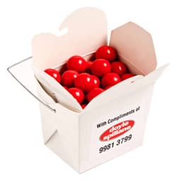 A white cardboard noodle box filled with bright orange chocolate drops. The box has a handle and a branding logo.