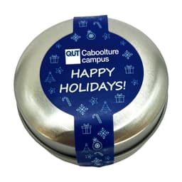 A round, silver candle tin featuring a blue label with festive designs and a holiday greeting.