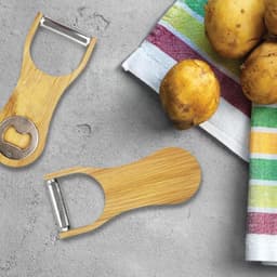 A drink bottle opener and peeler made from bamboo, featuring a metal bottle opener and surrounded by potatoes and a striped cloth.