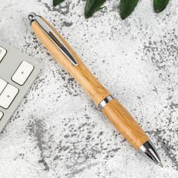 A bamboo pen with metal accents resting on a textured surface near a keyboard and greenery.