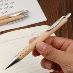 A pen with a wooden body and silver accents, held in a hand above a lined notebook.