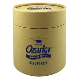 A drink bottle in a small, cylindrical gift tube made of brown cardboard, featuring a logo and blue text.