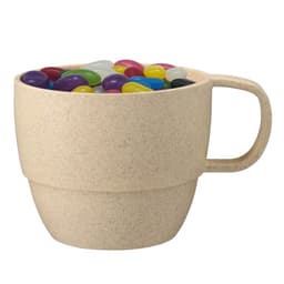 A reusable wheat straw cup in a light beige colour filled with colourful jelly beans. It features a handle and a logo.