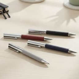 A collection of Geneva Metal Pens in grey, maroon, navy, and black with stainless steel accents, arranged on a desk.