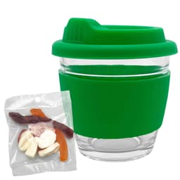 A green glass coffee cup with a silicone lid and sleeve, accompanied by a packet of mixed lollies in various colours.