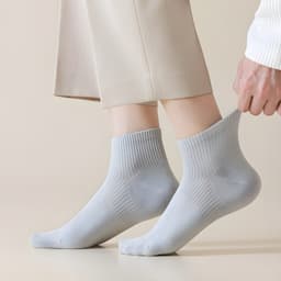 A pair of light grey socks is being pulled up, showcasing a ribbed design. The background is a neutral tone.