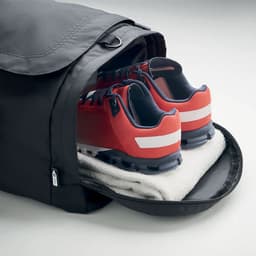 A black duffle bag with red shoes and a towel visible inside, featuring a logo on the side.