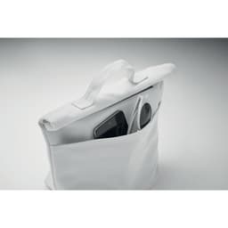 A white tote bag features an exterior pocket holding a smartphone and sunglasses. The bag has a sturdy handle.