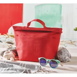 A red tote bag with a handle sits on a sandy surface next to rocks and a pair of green sunglasses.