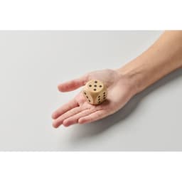 A hand holding a wooden dice with black dots on its sides against a plain background.