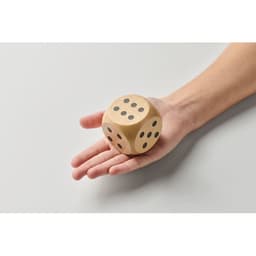 A wooden dice resting in a hand featuring black dots on each face. The background is plain and light.