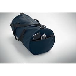 A duffel bag in navy blue with a zippered pocket containing a smartphone and a portable charger, featuring adjustable straps.
