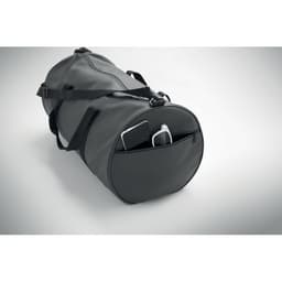 A grey duffle bag with a zipper pocket, containing a phone and a charger, featuring two carry handles and a shoulder strap.