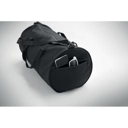 A black duffle bag with a side pocket containing a phone and a white device, featuring adjustable straps.