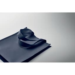 A dark blue tote bag with contrasting straps lies on a lightly textured surface, featuring a minimalistic design.