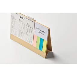 A desk calendar with a gold stand, featuring monthly pages and colourful sticky notes in pink, green, and blue.