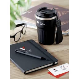 A drink bottle in black with a handle, next to a notebook, pen, glasses, and business cards on a wooden table.