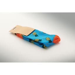 A pair of blue socks featuring pineapple patterns with orange accents, packaged with a cardboard tag.