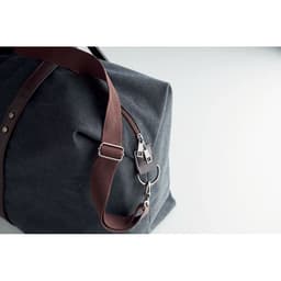 A duffle bag in dark grey fabric with a brown leather strap and metal hardware for secure closure.