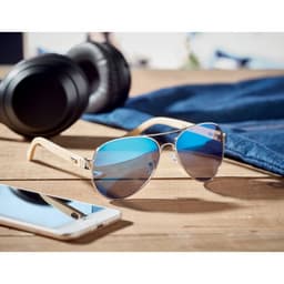 Sunglasses with a gold frame and blue-tinted lenses placed on a wooden surface, with headphones and a phone nearby.