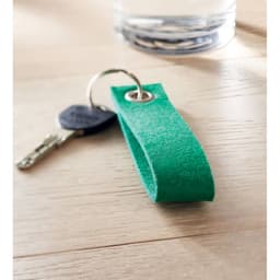 A green keychain with a loop for attaching keys, resting on a wooden surface next to a glass of water.