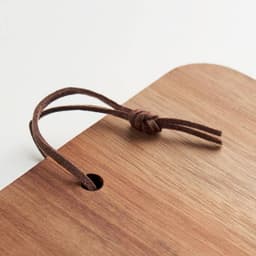 A wooden board with a rounded edge and a brown leather tie attached through a hole. The surface has a natural finish.