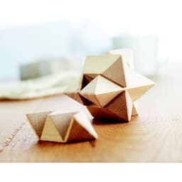 A set of wooden geometric shapes in natural tones, arranged on a wooden surface. The shapes feature a mix of pyramids and polyhedra.