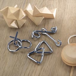 A collection of metal brain teaser puzzles and wooden geometric shapes arranged on a wooden surface.